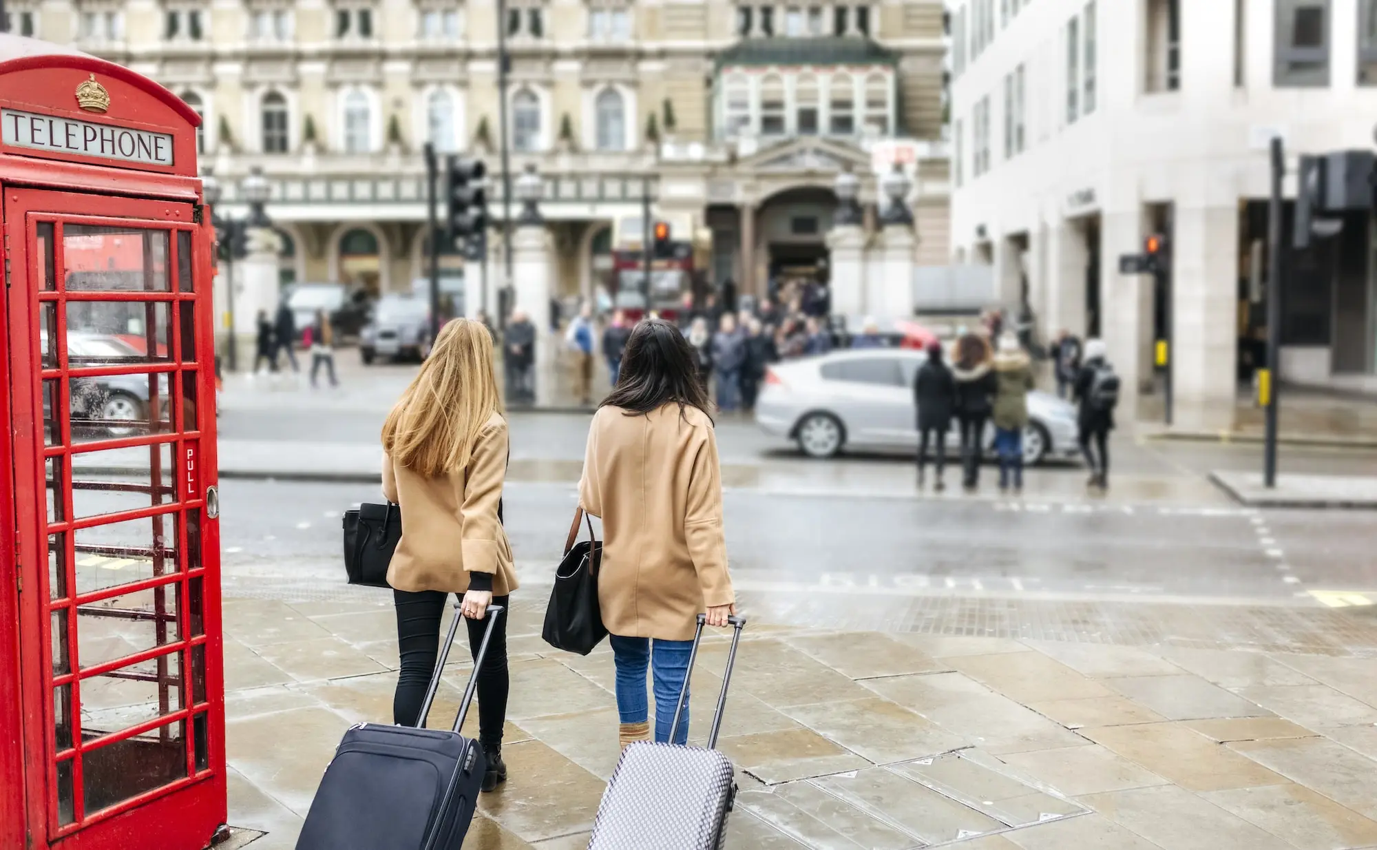 Photograph of two women with roller suitcases crossing a busy street in London.